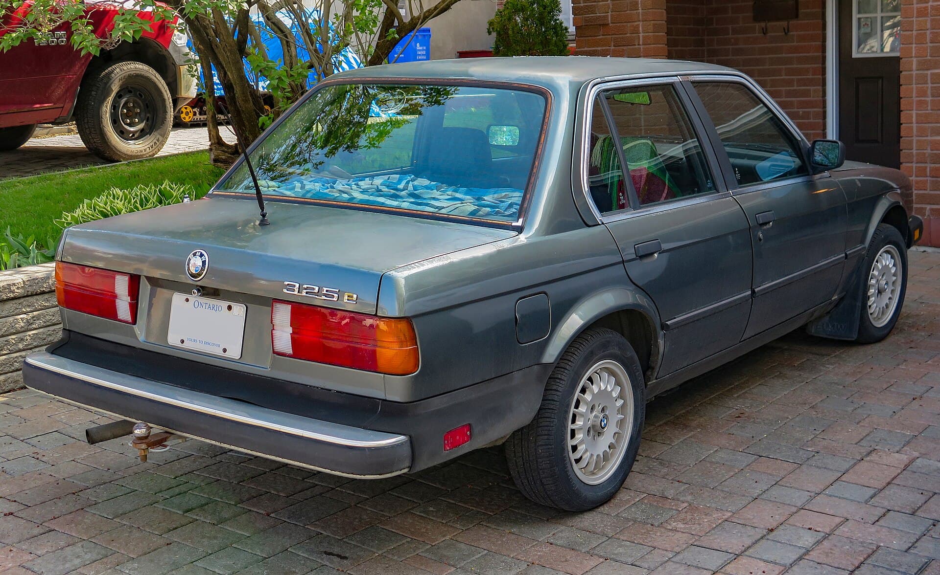 Grey 1985 BMW 325e four-door sedan on a brick driveway, seen from the rear