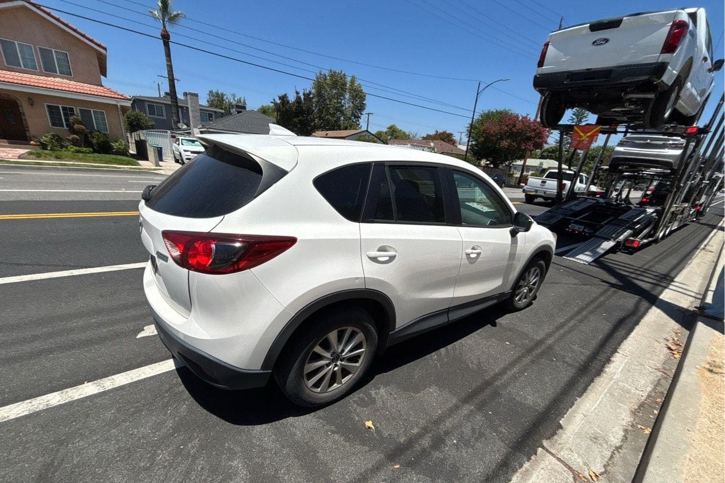 White Mazda CX-5 at the curb beside an open car carrier, seen from the rear quarter